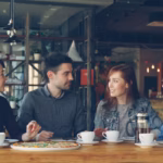 Group of people in warm animated conversation at a table — representing the social connection that supports recovery from anxiety