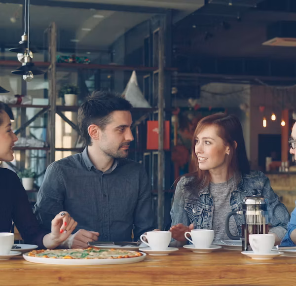 Group of people in warm animated conversation at a table — representing the social connection that supports recovery from anxiety